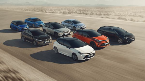 Acht verschiedenfarbige Toyota Modelle fahren in der Gruppe auf einem breiten Rollfeld in einer Wüste, leicht erhöht von vorn fotografiert
