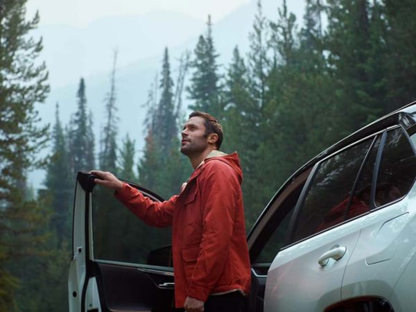 Eine Person steigt aus einem weißen Auto aus und blickt auf die Wälder um sie herum.