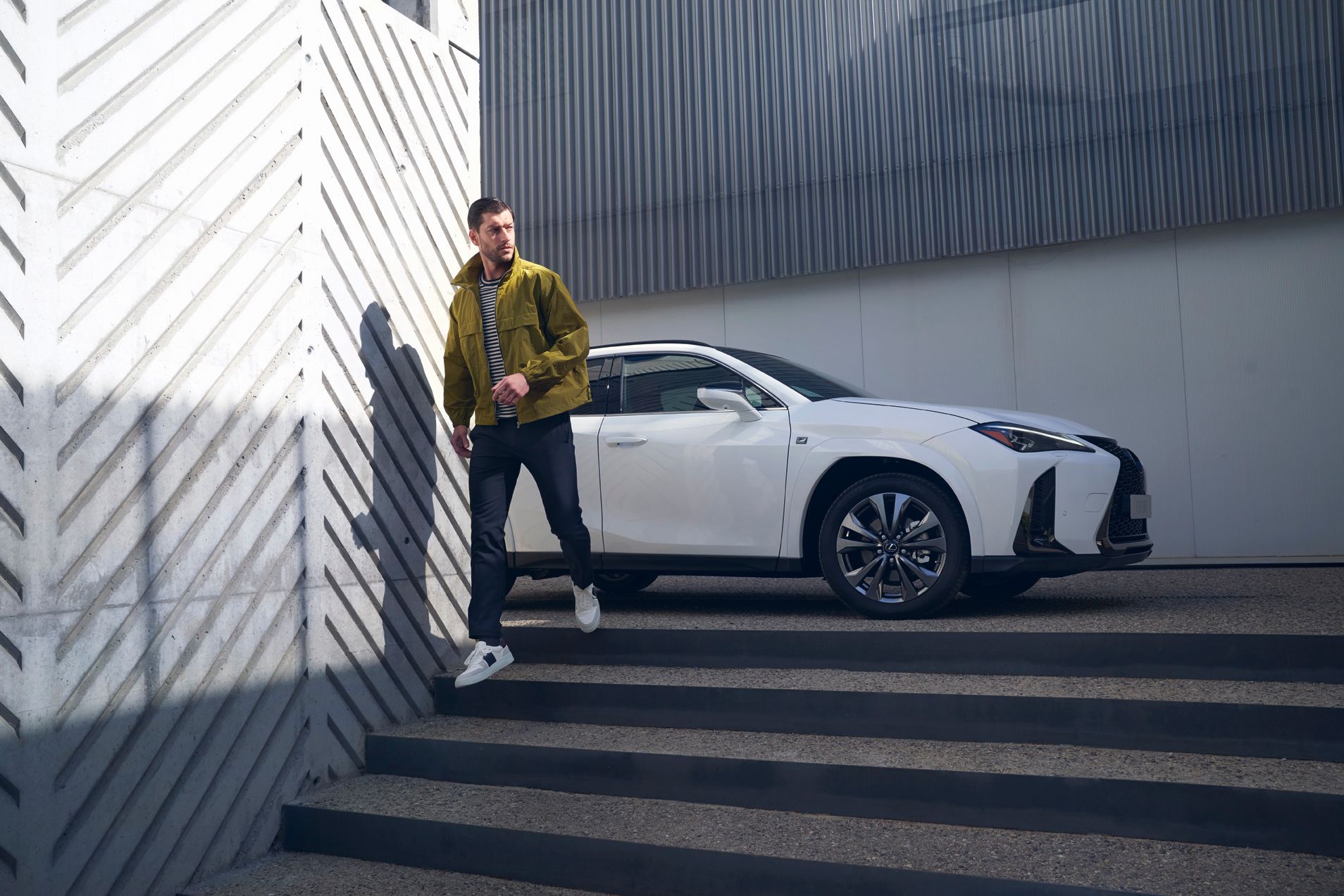 Ein Mann in grüner Jacke geht die Treppe neben einem eleganten weißen Lexus hinunter, der in einer modernen architektonischen
