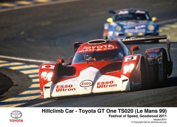 Ein rot-weißer Toyota GT One TS020-Rennwagen fährt beim Goodwood Festival of Speed durch eine Kurve, im Hintergrund ist ein weiteres Auto zu sehen.