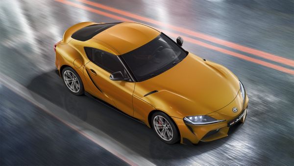 Sicht auf einen gelben Toyota GR Supra von schräg oben, der auf einer nassen Fahrban fährt