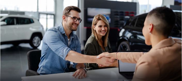 Dwoje uśmiechniętych klientów siedzi przy biurku z pracownikiem salonu Toyoty.