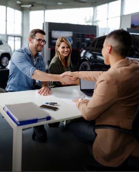 Dwoje uśmiechniętych klientów siedzi przy biurku z pracownikiem salonu Toyoty.