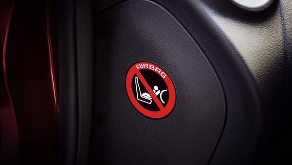 Warnaufkleber im Auto mit Symbol zur Deaktivierung des Beifahrer-Airbags bei rückwärtsgerichtetem Kindersitz.