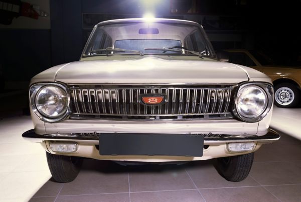 Frontansicht eines crèmefarbenen Corolla von 1967 mit verchromtem Kühlergrill, runden Schweinwerfern und einem alten, roten Toyota Logo 