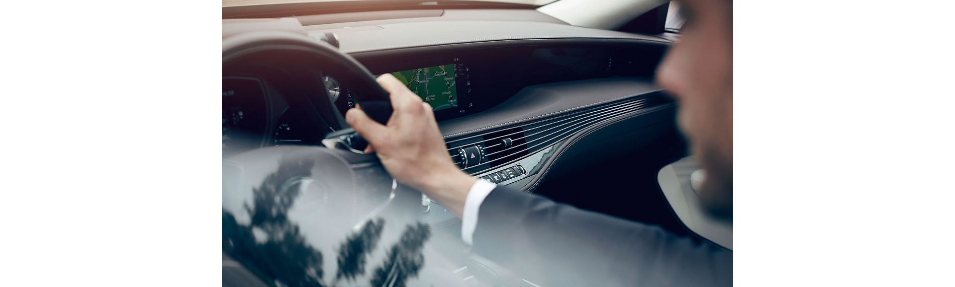 Eine Person im Anzug fährt einen Lexus LS, hält das Lenkrad fest und navigiert über eine digitale Kartenanzeige auf dem Armaturenbrett.
