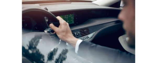 Eine Person im Anzug fährt einen Lexus LS, hält das Lenkrad fest und navigiert über eine digitale Kartenanzeige auf dem Armaturenbrett.