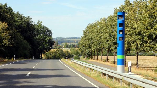 Eine blaue Säule zur Mauterfassung ist am Fahrbahnrand deutlich zu erkennen und fügt sich in die ländliche Umgebung mit Feldern und Bäumen ein.