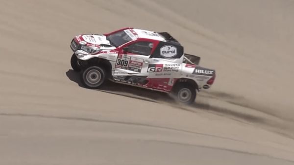 Rallye-Fahrzeug mit Toyota Logo und einer Folierung mit Sponsoren fährt auf einer Sanddüne