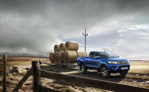 Blauer Toyota Hilux zieht einen Anhänger mit Strohballen durch eine karge Landschaft