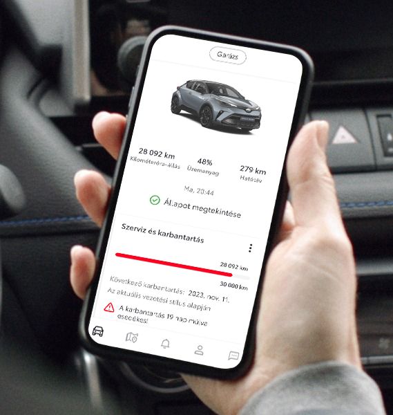 Kéz okostelefont tart egy autóban. A telefon képernyőjén egy szürke Toyota SUV képe látható, az autó kilométeróra állásával, üzemanyagszintjével és karbantartási információival.