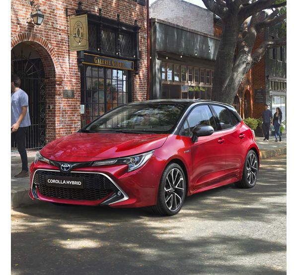 Roter Toyota Corolla Hybrid steht geparkt am Straßenrand unter Bäumen