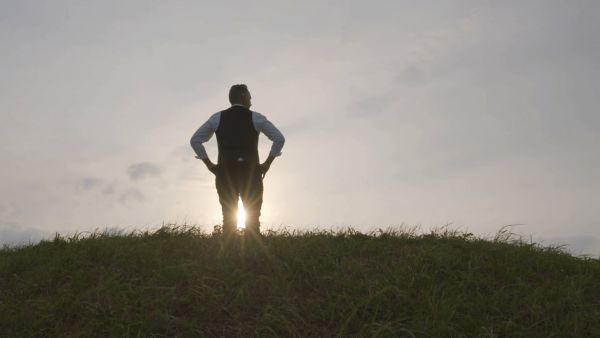 Person steht am Gipfel eines Hügels und schaut auf den Sonnenuntergang