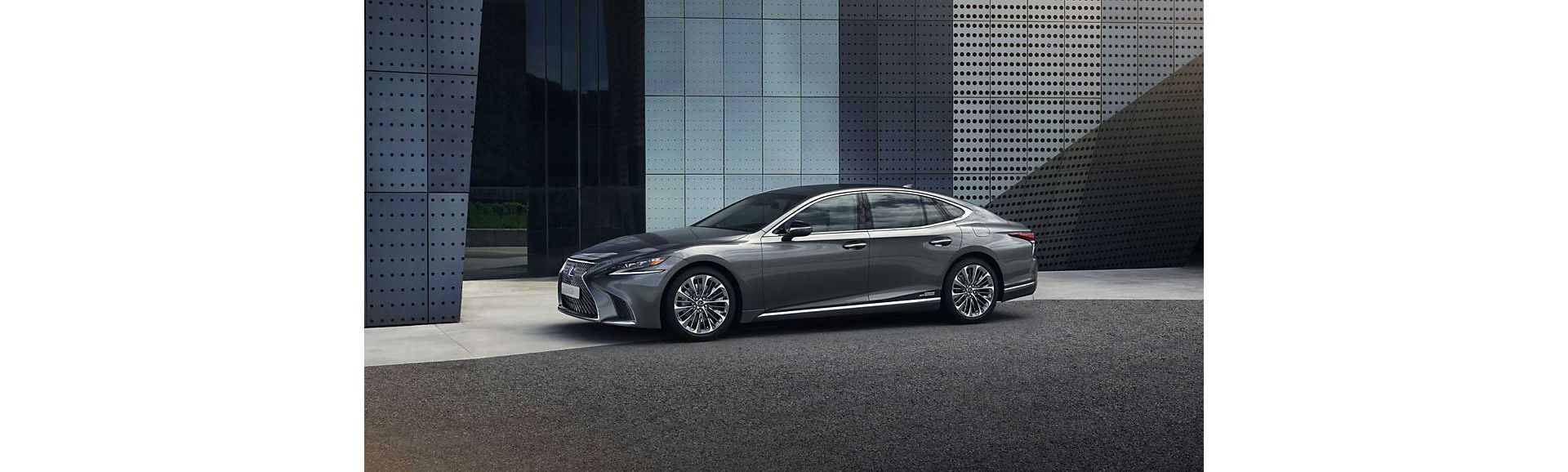 Ein eleganter grauer Lexus LS, der vor einem modernen Gebäude mit einer Glasfassade geparkt ist und sein stilvolles Design und seine Chromakzente zur Schau stellt.