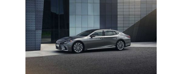 Ein eleganter grauer Lexus LS, der vor einem modernen Gebäude mit einer Glasfassade geparkt ist und sein stilvolles Design und seine Chromakzente zur Schau stellt.
