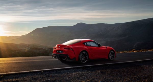 Ein roter Toyota Supra auf einer Landstraße. Im Hintergrund Berge.