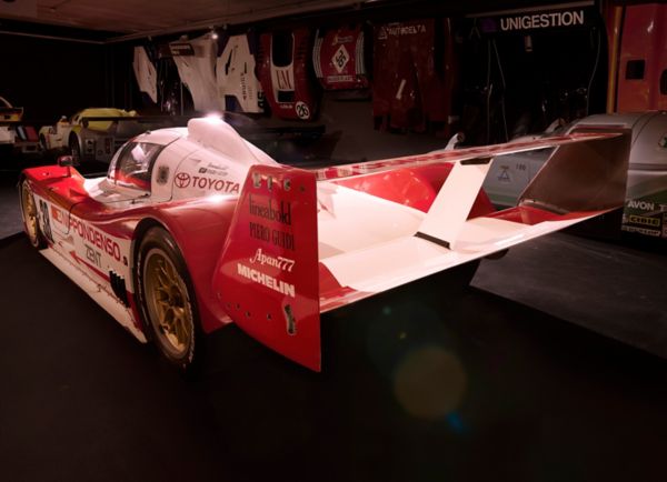 Weiß-roter TS010 Rennwagen mit Toyota Schriftzug und verschiedenen Sponsoren-Logos von schräg hinten, angestrahlt in einem dunklen Ausstellungsraum
