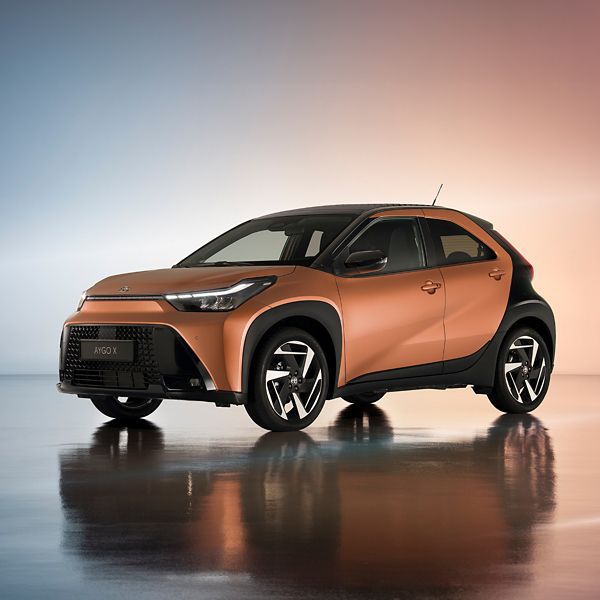 Ein orange farbender Toyota Aygo X auf einem bunten Hintergrund.