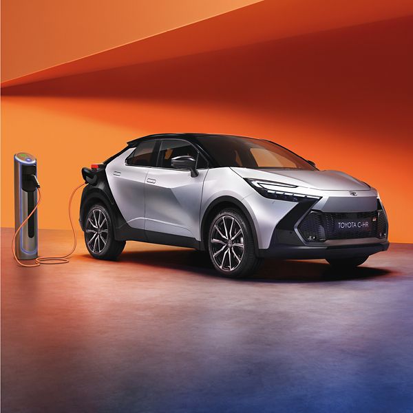 Ein silber Toyota C-HR an einer Ladesäule auf einem bunten Hintergrund.