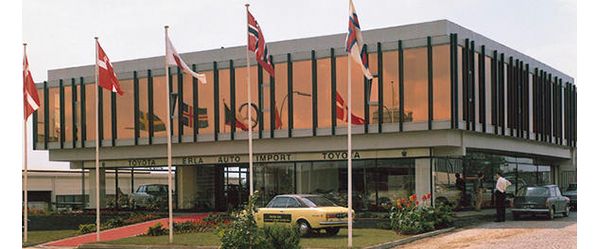 Farbfoto aus den 60er-Jahren: ein Autohaus mit den Schriftzügen „Erla“ „Auto“ „Import“ „Toyota“, davor Fahrzeuge, Personen und Fahnenmasten