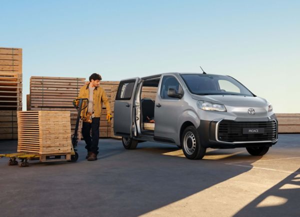 Ein junger Mann in Arbeitskleidung lädt mit einem Hubwagen Holzpaletten durch die geöffnete Schiebetür in einen Proace Transporter.