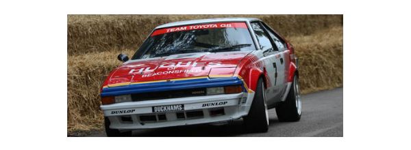Ein roter Rallyewagen mit "Team Toyota GB" auf der Frontscheibe und Heuballen daneben.