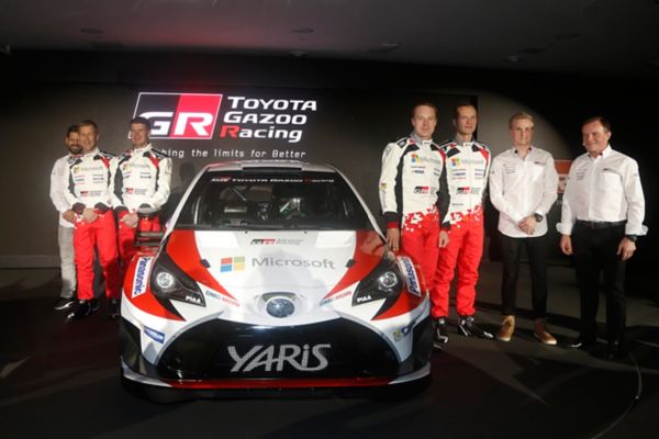 Das Toyota Gazoo Racing Team steht neben einem Toyota Yaris Rallye-Auto. Im Hintergrund ist das Toyota Gazoo Racing Logo zu sehen.