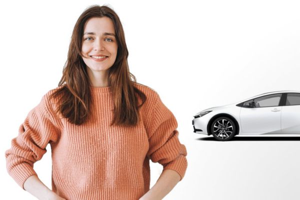 Lächelnde Frau steht mit Armen an den Hüften und einem weißen E-Auto hinter ihr vor einem weißem Hintergrund.