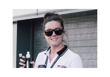 Portrait von Abbie Eaton in weißem T-Shirt, schwarzer Sonnenbrille und Getränk in der Hand.