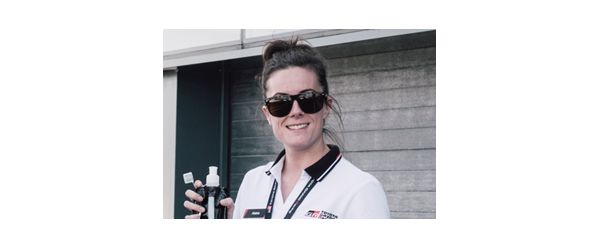 Portrait von Abbie Eaton in weißem T-Shirt, schwarzer Sonnenbrille und Getränk in der Hand.