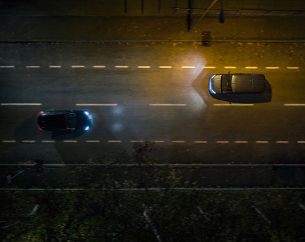 Perspektive von oben auf eine Straße bei Nacht, auf der sich zwei Fahrzeuge entgegenkommen