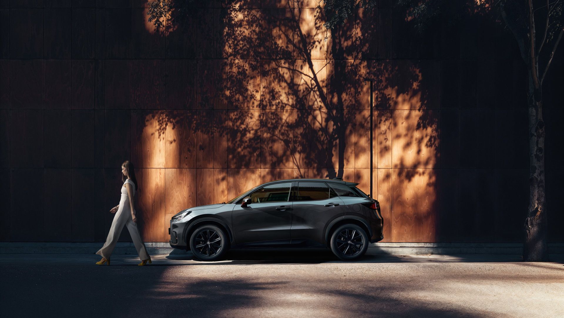 Una persona cammina accanto a un Lexus LBX Vibrant Edition parcheggiato.