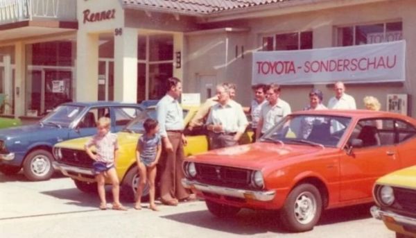 Viele Personen stehen neben einem roten Toyota aus dem Jahr 1979 