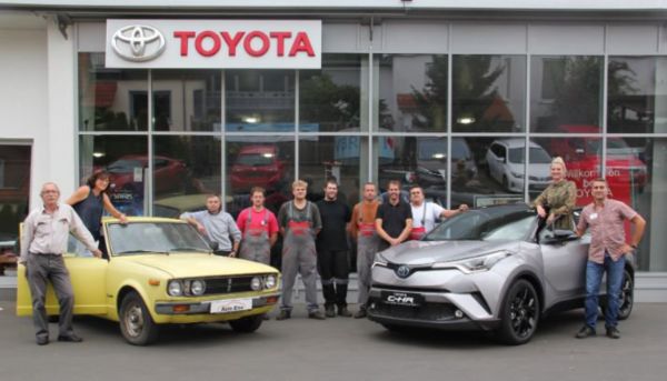 Ein Teambild der Auto Eise GmbH vor dem Toyota Autohaus mit zwei Fahrzeugen. Links ein alter Toyota in gelb und rechts ein silberner Toyota C-HR