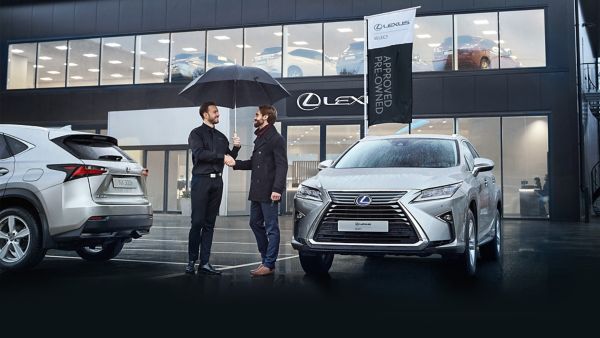 Een Lexus-adviseur en een klant schudden elkaar de hand voor een Lexus-dealer.