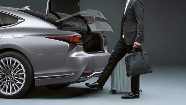 Eine Person mit zwei Taschen in den Händen bedient den Fußsensor der Kofferraumklappe eines Lexus LS