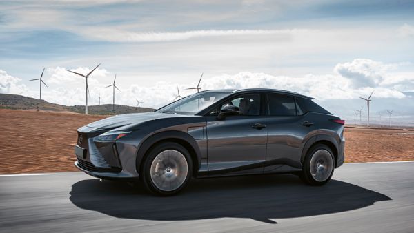 Ein dunkelgrauer Lexus RZ fährt auf einer Straße mit Windrädern im Hintergrund