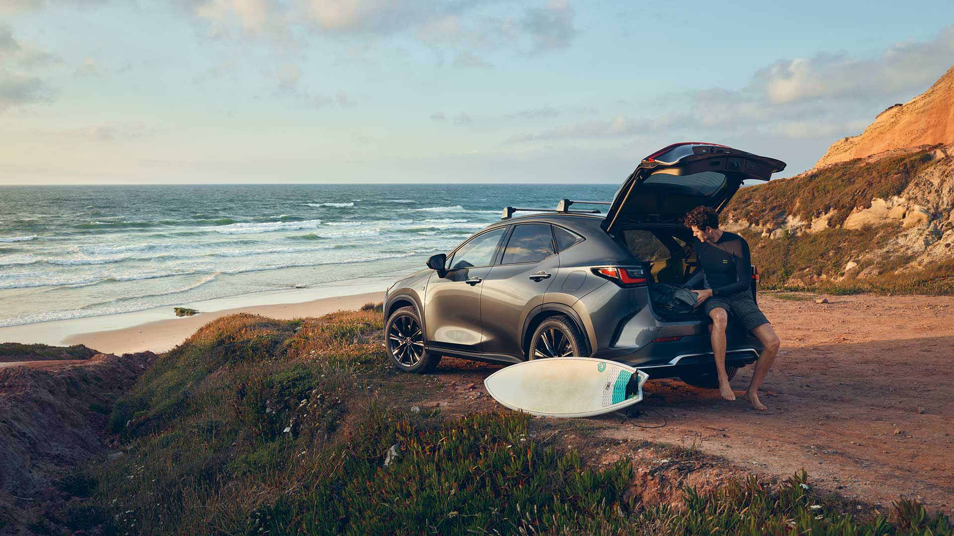 A man sat on the boot of the Lexus NX on the coast