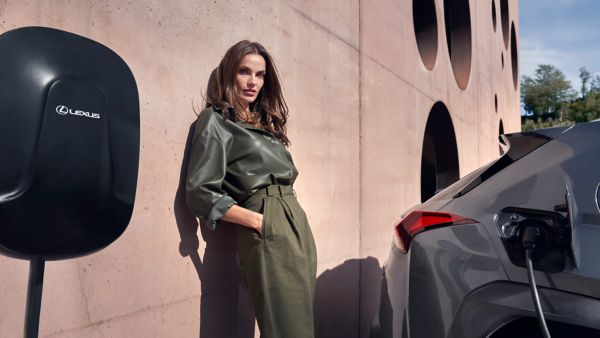 Eine Frau lehnt an einer Wand während neben ihr ein geparkter Lexus an einer Wallbox lädt