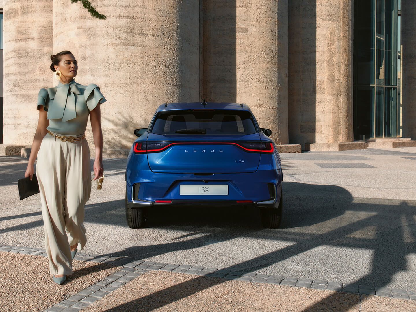 A Women walking behind a Blue Lexus LBX model