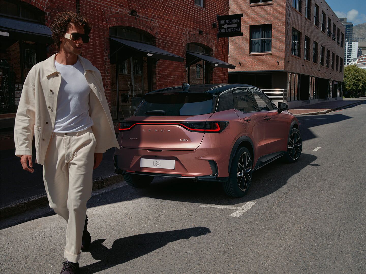 A man walking behind a brown Lexus LBX model
