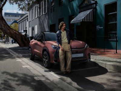 Ein Mann steht lässig neben einem Lexus LBX, das in einer ruhigen Straße geparkt ist