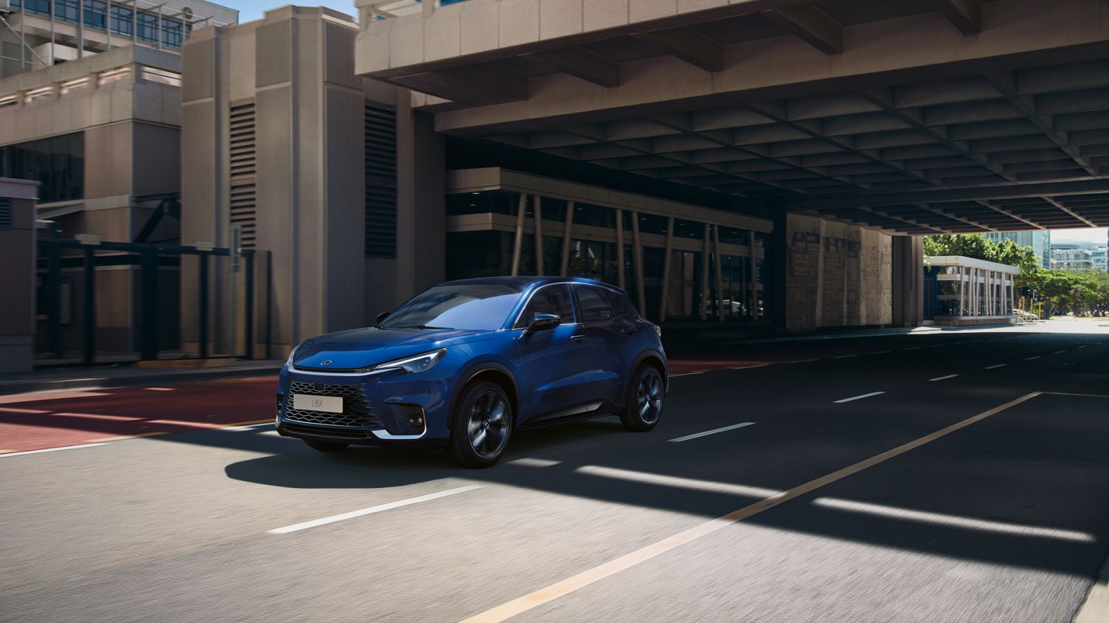 Ein blauer Lexus LBX SUV fährt durch ein Stadtgebiet unter einer Betonüberführung