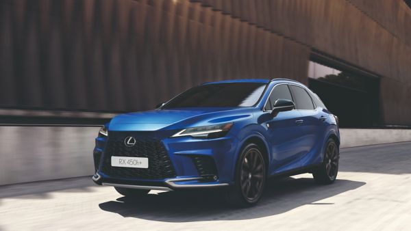 Ein blauer Lexus RX 450h fährt entlang einer modernen Fassade