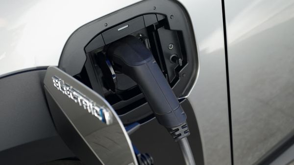 Eine Detailaufnahme zeigt den Ladeanschluss eines silbernen Elektroautos mit eingestecktem schwarzen Ladekabel. Auf der geöffneten Klappe steht in glänzenden Buchstaben das Wort „ELECTRIC“. Das Bild symbolisiert das elektrische Laden eines Fahrzeugs, bei dem für den Zugang zur Ladestation häufig eine Ladekarte für Elektroautos erforderlich ist.