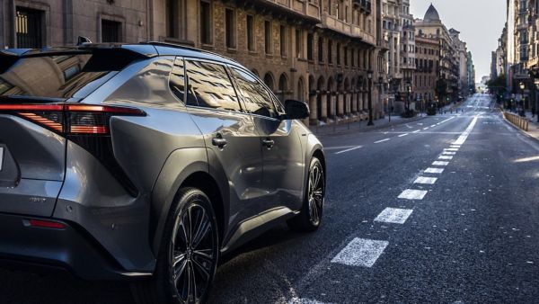 Heckansicht eines rechts angeschnittenen grau silbernen Toyota bZ4X, der eine Stadtstraße runter fährt mit historischen Gebäuden und Ampeln in der Ferne.