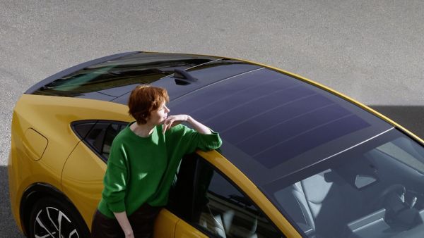 Vogelperspektive auf eine Frau, die sich an dem Solardach eines gelben Prius Plug-In Hybrid anlehnt.