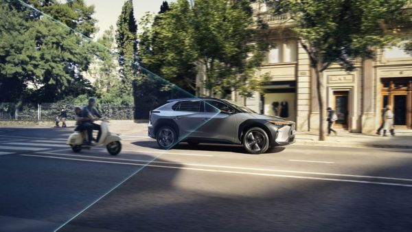 Ein Toyota bZ4X fährt durch die Stadt, schräg dahinter ein Motorroller, im grafisch eingeblendeten Überwachungsbereich des Totwinkel-Assistenten