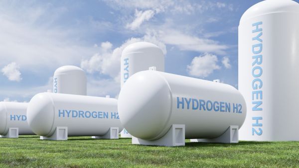 Mehrere weiße Tanks mit der Aufschrift "Hydrogen H2" stehen auf einem Rasen unter blauem Himmel
