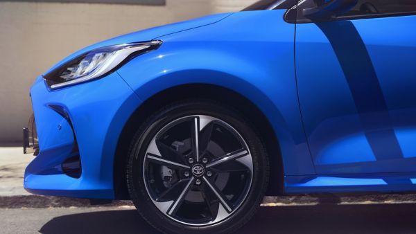 Nahaufnahme von der Seite eines blauen Yaris mit dem Fokus auf die vorderen Felgen und Scheinwerfer.